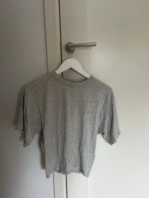 Ljusgrå basic t-shirt - En enkel ljusgrå t-shirt i mjuk bomull med normal passform och korta ärmar. Perfekt till jeans eller shorts för en avslappnad look. Tajt runt midjan men lösare upptill