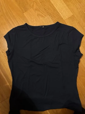 Mörkblå enkel t-shirt - En basic mörkblå t-shirt med rund hals och korta ärmar. Perfekt till jeans eller shorts och lätt att matcha med andra plagg. Tillverkad i mjuk bomull för skön känsla hela dagen.