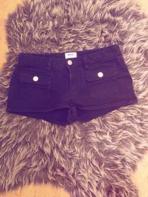 Svarta monki jeans shorts - shortsen är ett par stilrena svarta minishorts i ett stadigt, jeansliknande material som ger en snygg och strukturerad passform. De har en låg till medelhög midja med klassisk knappstängning och dragkedja framtill