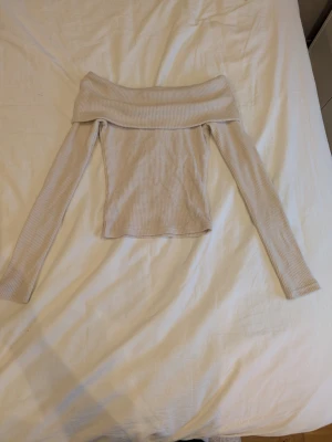 Beige offshoulder topp Gina Tricot - Trendig beige offshoulder topp från Gina Tricot i ribbad bomullsmix. Långärmad och figurnära passform med bred kant upptill som ger en snygg siluett. Perfekt att styla med jeans eller kjol.