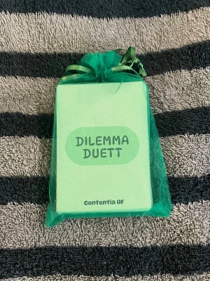 Dilemma Duett kortspel - Dilemma Duett är ett svenskt kortspel från Contentia UF där spelare ställs inför olika dilemman och argumenterar för sina val. Korten är ljusgröna med mörkare text och rundade hörn. Perfekt för spelkvällar med vänner och familj! 😝OBS färgen på korten ser lite annurlunda ut på de första bilderna, men de sista två visar den riktiga färgen i dagsljuset 🤗