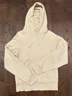 Acne Studios Hoodie Mens xs Beige - Snygg beige hoodie från Acne Studios med klassisk huva och vita dragsnören. Hoodien har en känguruficka framtill och den ikoniska Acne Studios-loggan broderad på bröstet. Tillverkad i mjuk bomullsblandning för maximal komfort och stil.