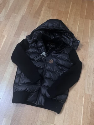 Marcél Classic 02 Svart Hybrid Jacka - Quiltad pufferkropp, stickade ärmar, helzip, avtagbarluva. Lapp kvar, utmärkt skick. Köp med Klarna på www.cain.se eller DM:a mig här! 🤝​​​​​​​​​​​​​​​​