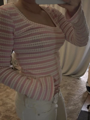 Rosa och vit stickad topp - Söt stickad topp i rosa och vitt med horisontella ränder och strukturmönster. Rundad, bred ringning och halvlånga ärmar. Perfekt för dig som gillar en mjuk och retroinspirerad look. Materialet känns mjukt och stretchigt.