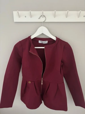 Vinröd kavaj/kofta - Stilren vinröd kavaj/kofta från Chiara Forthi med rund halsringning och dragkedja framtill. 