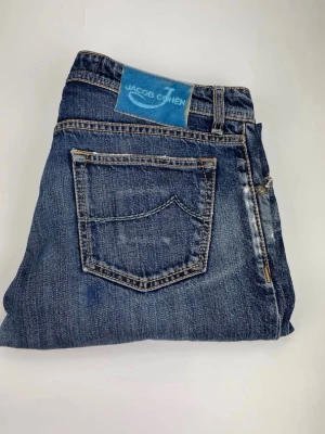 Blå jeans från Jacob Cohen - Snygga blå jeans från Jacob Cohen med klassisk femficksmodell och raka ben. Jeansen har en tvättad look med slitningar och kontrastsömmar. Tillverkade i mjukt denimtyg som ger en skön känsla och passar perfekt till en avslappnad stil.