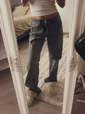Gråa raka jeans med låg midja - Säljer ett par gråa jeans med rak passform och låg midja. Jeansen har klassisk femficksdesign och stängs med knapp och dragkedja. Perfekta för en avslappnad och trendig look.