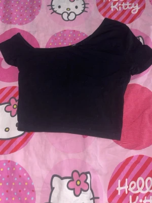 Svart off shoulder crop top - Trendig svart crop top med off shoulder-design och korta ärmar. Toppen har en tight passform och är perfekt för att styla med höga jeans eller kjol. Materialet känns mjukt och stretchigt, vilket gör den bekväm att bära hela dagen.