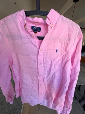Rosa linneskjorta från Polo Ralph Lauren🙌🤩 - Säljer en ljusrosa skjorta från Polo Ralph Lauren i linne med klassisk krage och knappar framtill. Skjortan har lång ärm och den ikoniska blå loggan broderad på bröstet. Perfekt för en avslappnad men ändå stilren look.🙌🤩