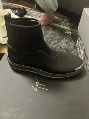 Svarta stövletter från Giuseppe Zanotti - Snygga svarta stövletter från Giuseppe Zanotti i slätt läder med dragkedja framtill och dekorativ metall-detalj på tån. Sulan har kontrastsömmar och ger en modern touch. Perfekta för dig som vill ha en stilren och exklusiv look.