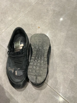 Valentino Garavani Rockrunner sneakers - Snygga Valentino Garavani Rockrunner sneakers i svart med camouflage-mönster i grått, beige och grönt. Skorna har snörning, rund tå och platt sula. Tillverkade i en mix av skinn och mocka för en lyxig känsla. Kommer med originalkartong, dustbag och extra skosnören. Några skavanker på sko och låda därav priset