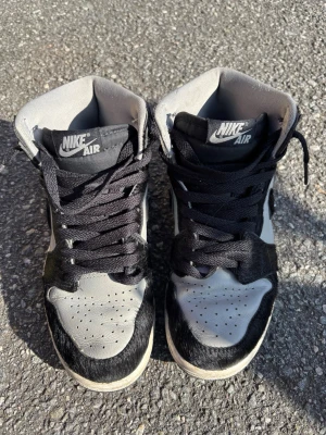 Nike Air Jordan 1 High svart/vit - Säljer ett par Nike Air Jordan 1 High sneakers i svart och vitt. Skorna har svart Swoosh, svarta snören och detaljer i mocka med en unik hårig textur. Klassisk hög siluett och perforerad tåbox för extra stilpoäng.