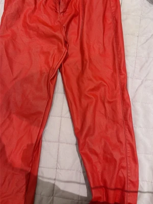 Röda leggings i skinnimitation - Snygga röda leggings i skinnimitation med hög midja och smal passform. Materialet har en glansig finish som ger en cool look. Perfekta att styla med oversized tröja eller crop top för en trendig outfit.