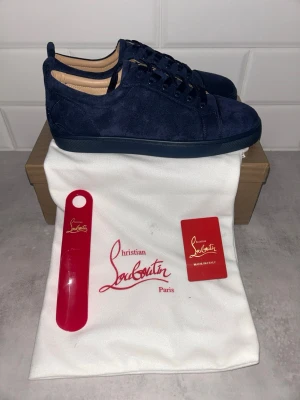 Mörkblå sneakers Christian Louboutin - Snygga mörkblå sneakers Christian Louboutin i mjukt mockaskinn. Klassisk låg modell med matchande mörkblå snörning och sula. Perfekta för dig som vill ha en stilren och exklusiv look. Kommer med påse och tillbehör.