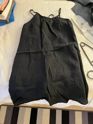 Svart ärmlös sommarklänning - En enkel svart klänning med tunna axelband och rak passform. Perfekt för varma dagar och lätt att styla med accessoarer. Tillverkad i ett mjukt och luftigt material som känns skönt mot huden.