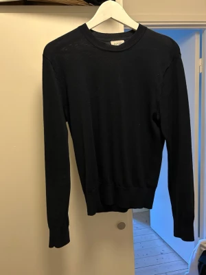 Svart stickad tröja från Sandö - Klassisk svart stickad tröja från Sandö med rund halsringning och långa ärmar. Tröjan har ribbade muddar vid ärmslut och nederkant, vilket ger en snygg och enkel look. Perfekt att matcha med jeans. Har ett litet hål på ryggen, kolla sista bilden 