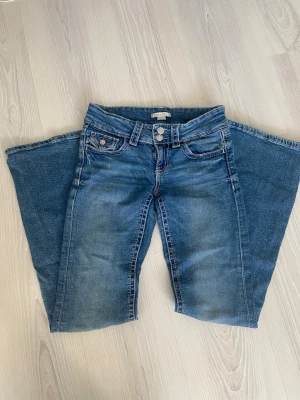 Blå bootcut jeans med slitningar - Säljer ett par blå bootcut jeans med snygga slitningar och klassisk femficksmodell. Jeansen har en låg midja. Perfekta för en avslappnad och trendig look. Storlek 152 jätte fint skick!