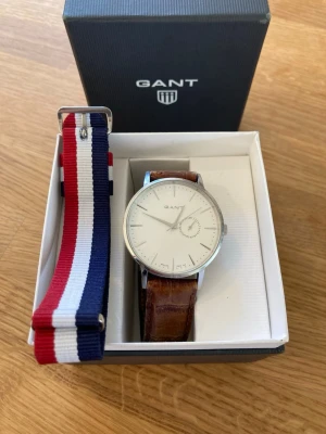 Gant Park Hill 42mm Herrklocka - Säljer en snygg stilren herrklocka från modejätten GANT i nära nyskick enligt bilder. Finns små tunna repor på glaset som inte syns. Fungerar bra, originalarmband i äkta läder lite slitet, datumvisare, japanskt urverk, vattentät osv. Behöver bara nytt batteri. Fås i original box med certifikat och extra armband (ej original).  Nypris: 1900 SEK Begagnat pris: 1000 SEK Mitt pris: 589 SEK  Skickas alltid snabbt och spårbart. Skriv vid frågor och se gärna mina andra annonser!   GRATIS: För betalande