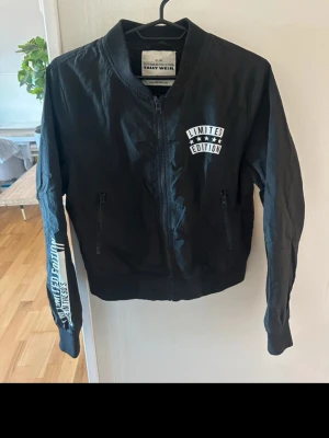 Svart bomberjacka Limited Edition storlek 38 - Cool svart bomberjacka från Italy Wear med tryck 'Limited Edition' på bröstet och ärmen. Jackan har ribbade muddar, dragkedja framtill och två fickor med dragkedja. Materialet är lätt och passar perfekt för en trendig streetstyle-look.
