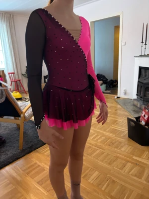 Glittrig konståkningsklänning rosa/svart - Konståkningsklänning av sömmerska. Passar någon som är ca 155-160 cm. Är 168 cm på bilden. Säljs på grund av storlek och bytt program. Lagad på arm 