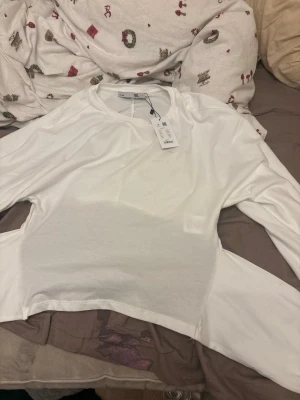 Vit långärmad topp från lager 157 - Säljer en enkel och stilren vit långärmad topp från lager 157. Toppen har rund halsringning och är gjord i ett mjukt material som känns skönt mot huden. Perfekt att matcha med jeans eller kjol för en clean look.