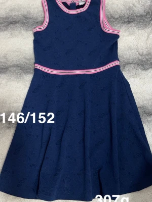 Marinblå klänning med rosa detaljer - Snygg marinblå klänning med rosa och vita ränder vid halsringning, ärmhål och midja. Ärmlös modell med rund hals och lätt utställd kjol. Perfekt för dig som gillar sportig men söt stil.🌸 Använd två gånger. Storlek 146/152