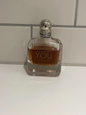 Stronger With You Intensely parfym - En snygg parfymflaska från Emporio Armani, Stronger With You Intensely. Flaskan är genomskinlig med en fyrkantig form och innehåller en bärnstensfärgad vätska. Perfekt för dig som gillar eleganta och moderna dofter.