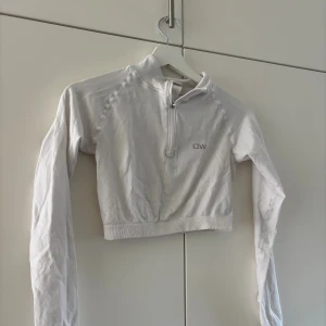 Vit cropped träningströja från ICANIWILL - Snygg vit långärmad cropped träningströja från ICANIWILL med halv dragkedja framtill och diskret logga på bröstet. Tillverkad i stretchigt funktionsmaterial som passar perfekt till gymmet eller löprundan. Passar nog även S