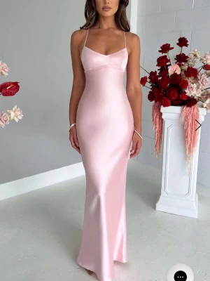 Ljusrosa långklänning i satin - Elegant ljusrosa långklänning i satin med smala axelband och öppen rygg med snörning. Klänningen har en figurnära passform och ett mjukt, glansigt material som ger en lyxig känsla. Perfekt för speciella tillfällen. Säljer pågrund av att jag köpte fel storlek, klänningen är från Babyboo och jag har aldrig använt den. Jag är 173 cm lång och den går ända ner till marken. Perfekt för bal osv🥰