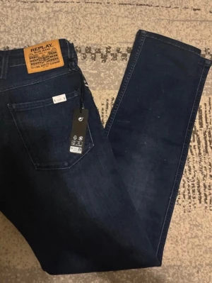 Mörkblå jeans från Replay - Snygga mörkblå jeans från Replay med klassisk femficksdesign och läderpatch bak i midjan. Jeansen har raka ben och är tillverkade i bomullsdenim med en stilren look. Perfekta för dig som gillar en tidlös och trendig stil.