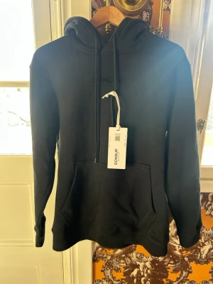 Svart hoodie från Dondup - Snygg svart hoodie från dundup med klassisk ficka och huva. Tillverkad i mjukt material som känns skönt mot huden. Diskret Dondup-logga framtill för en clean look. Perfekt för dig som gillar enkel och stilren look. Hoodien är helt ny med tags och har aldrig använts. Hör av er vid frågor. Priset är ej hugget i sten! 