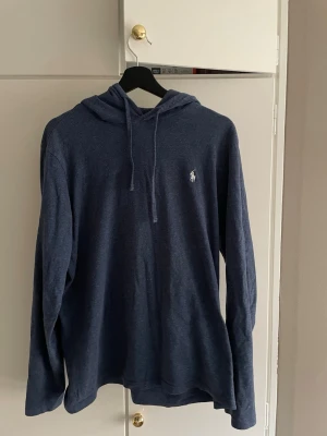 Mörkblå hoodie från Ralph Lauren - Snygg mörkblå hoodie från Ralph Lauren med luva. Tillverkad i mjukt och lätt material i storlek M. Vit Polo-logga broderad på bröstet. Långärmad och enkel design som passar till det mesta. Tveka inte att höra av dig om du har några frågor.