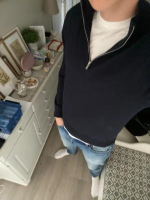 Mörkblå halvzip tröja - Snygg mörkblå tröja med halv dragkedja i halsen. Tröjan har en stilren och enkel design med långa ärmar och ribbade muddar. Perfekt att bära över en t-shirt för en avslappnad men ändå uppklädd look.