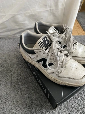 Vita New Balance 550 sneakers - Snygga New Balance 550 sneakers i vitt med svarta detaljer och klassisk N-logga på sidan. Skorna har lågt skaft, perforerad tå och är tillverkade i läder och textil. Perfekta för en sportig och trendig stil.