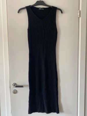 Svart ribbad långklänning från SHEIN - Svart långklänning från SHEIN i ribbstickat material. Klänningen är ärmlös med v-ringad hals och har en figurnära passform. Perfekt för dig som gillar en enkel och stilren look.