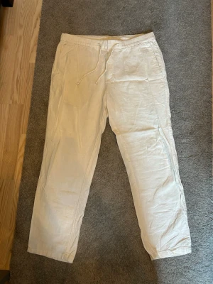 Beiga linnebyxor från H&M Regular Fit - Snygga beiga linnebyxor från H&M i regular fit. Byxorna har dragsko i midjan och raka ben, perfekta för en avslappnad och stilren look. Tillverkade i ett lätt och luftigt linnematerial som passar perfekt till varmare dagar.