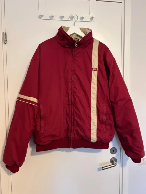 Röd vintage jacka med beige detaljer - Cool röd retrojacka med beigea ränder på ena ärmen och framtill. Jackan har hög krage, dragkedja och två fickor. Köpt begagnad på Vinted men har inte använts sedan dess.