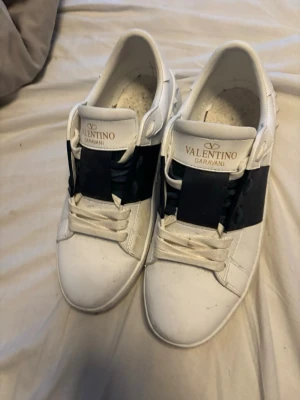 Valentino Garavani vita sneakers - Säljer ett par vita sneakers från Valentino Garavani med svart detalj över snörningen. Klassisk låg modell med rund tå och vita skosnören. Märkeslogga på plösen och stilren design som passar till det mesta.