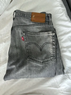 Grå Levi's jeans med rak passform - Säljer ett par grå jeans från Levi's med klassisk rak passform och femficksmodell. Jeansen har en snygg tvättad look, tydlig bakficka med V-söm och den ikoniska röda Levi's-lappen. Tillverkade i slitstark denim med läderpatch bak i midjan. I modellen 501. Storlek står ej fast sitter exakt som W 30 L 32. Raka 