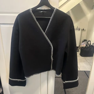 Svart kappa med vit kant - Stilren svart kappa från Gina Tricot med kontrasterande vit dekorationssöm längs kanterna och ärmsluten. Strl S🩷