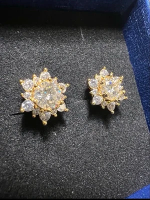 18 k Guldpläterade moissanite örhängen  - Säljer ett par glittriga moissanite örhängen i 18 k guldpläterad med gnistrande klara stenar i blomformad design. Örhängena har en stor mittsten omgiven av mindre stenar som ger en exklusiv och elegant look. Perfekta för dig som gillar att sticka ut med accessoarer. Testar Positivt på diamant testare 