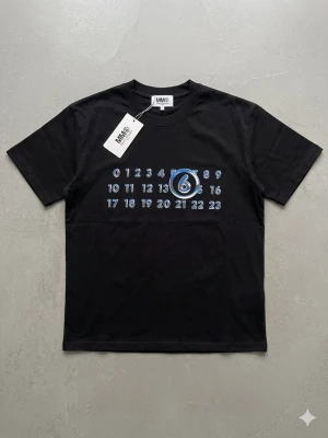 Svart t-shirt från MM6 Maison Margiela - Cool svart t-shirt från MM6 Maison Margiela med tryck av siffror och en blåmarkerad sexa på bröstet. Klassisk passform med rund hals och korta ärmar. Perfekt för dig som gillar streetwear och unika detaljer.