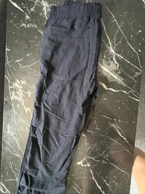 Mörkblå linnebyxor - Säljer ett par mörkblå linnebyxor med resår i midjan och bakficka. Byxorna har en avslappnad passform och är perfekta för chill dagar. Tillverkade i mjukt material som känns skönt mot huden.