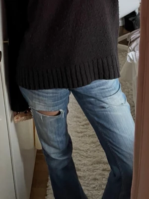 Lee jeans bootcut med hål - Säljer ett par blå bootcut jeans med slitningar. Jeansen har låg midja och klassisk femficksdesign. Perfekta för en avslappnad och trendig look.