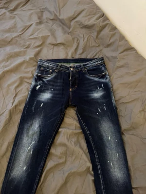  Dsquared2 jeans  - Snygga mörkblå jeans från Dsquared2 med coola slitningar och ljusa detaljer framtill. Klassisk femficksmodell med orange kontrastsömmar och Dsquared2-logga vid gylfen. Perfekta för en trendig streetwear-look.