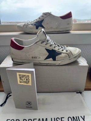Golden Goose  - Tjeneritz, säljer nu mina Golden Goose sneakers i vitt läder med mörkblå stjärna på sidan och röd hälflik. Skorna är köpta på MerchSweden för ett nypris på ca 4 599 SEK, skorna är i storlek 41⭐️        Nu säljs skorna för endast 1599kr, diskutertbart. Skicket är bra, det är dock lite defekter som syns om man kollar noga men inte vid användning. Första dagen jag hade skorna på mig fick jag grymt många komplimanger🙌                                                   Skriv till mig vid intresse📩❤️