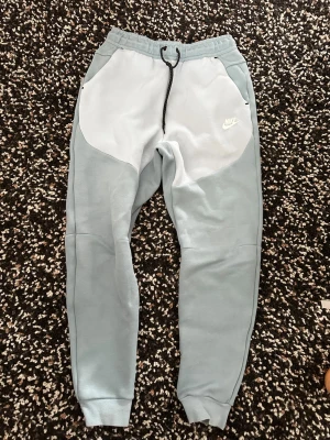 Nike tech ljusblå mjukisbyxor - Nike mjukisbyxor i ljusblått med vita detaljer. Finns en liten fläck men inget som syns tydligt