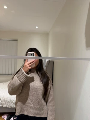 Beige stickad tröja med slits - Mysig beige stickad tröja med rund hals och breda ribbade muddar vid ärmslut och nederkant. Tröjan har en avslappnad passform och små slitsar i sidorna för extra komfort. Perfekt för lager-på-lager och enkel att matcha.