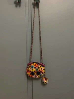 Färgglad fluffig väska/plånbok med djurmotiv - Supergullig väska/plånbok i form av ett djuransikte med färgglatt leopardmönster i gult, rosa, blått och lila. Väskan är gjord i mjukt, fluffigt material och har kedjerem med inslag av tyg. Perfekt för dig som vill sticka ut med en lekfull accessoar.💗