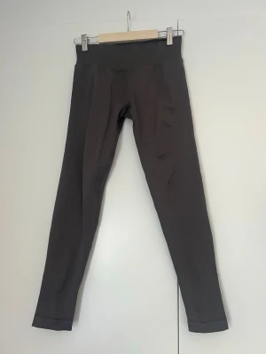 Träningstights  - Snygga Träningstights från Relode med medelhög midja och scrunch-detalj bak. De är tighta och stretchiga, perfekta för träning eller chill. Materialet är mjukt och följsamt, vilket ger en skön passform. Relode-logga baktill i vitt. En slags grå/brun färg. Inga tecken på användning!